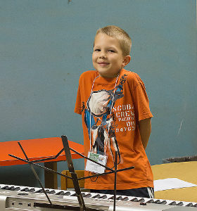 boy in orange shirt standing by keyboard